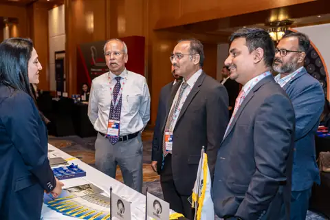 A group of delegates exchange information beside a conference exhibition table.