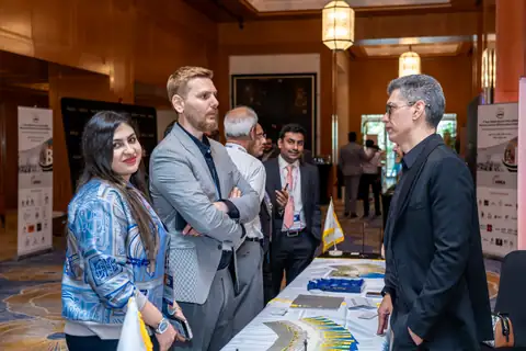 Attendees continue a discussion beside a table of brochures in a conference exhibition area.