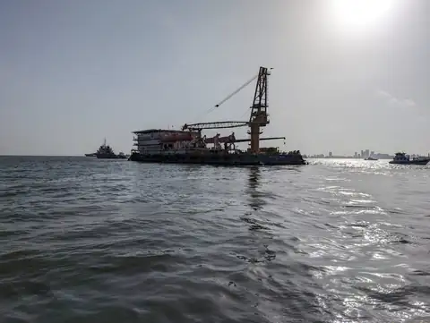 A crane vessel appears in silhouette on sunlit water, with smaller craft nearby.