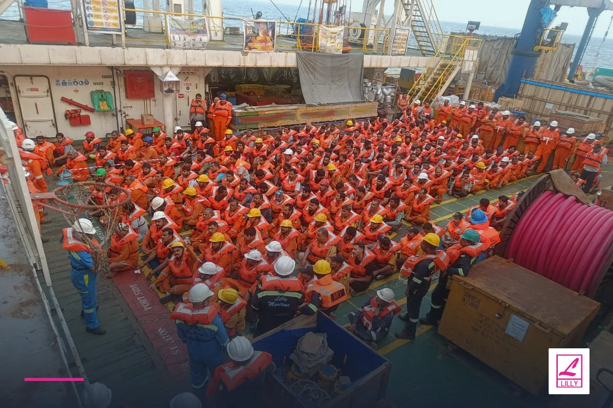 Crew in orange lifejackets and hard hats assembled across a vessel deck, with a navy and magenta Lilly Maritime treatment.